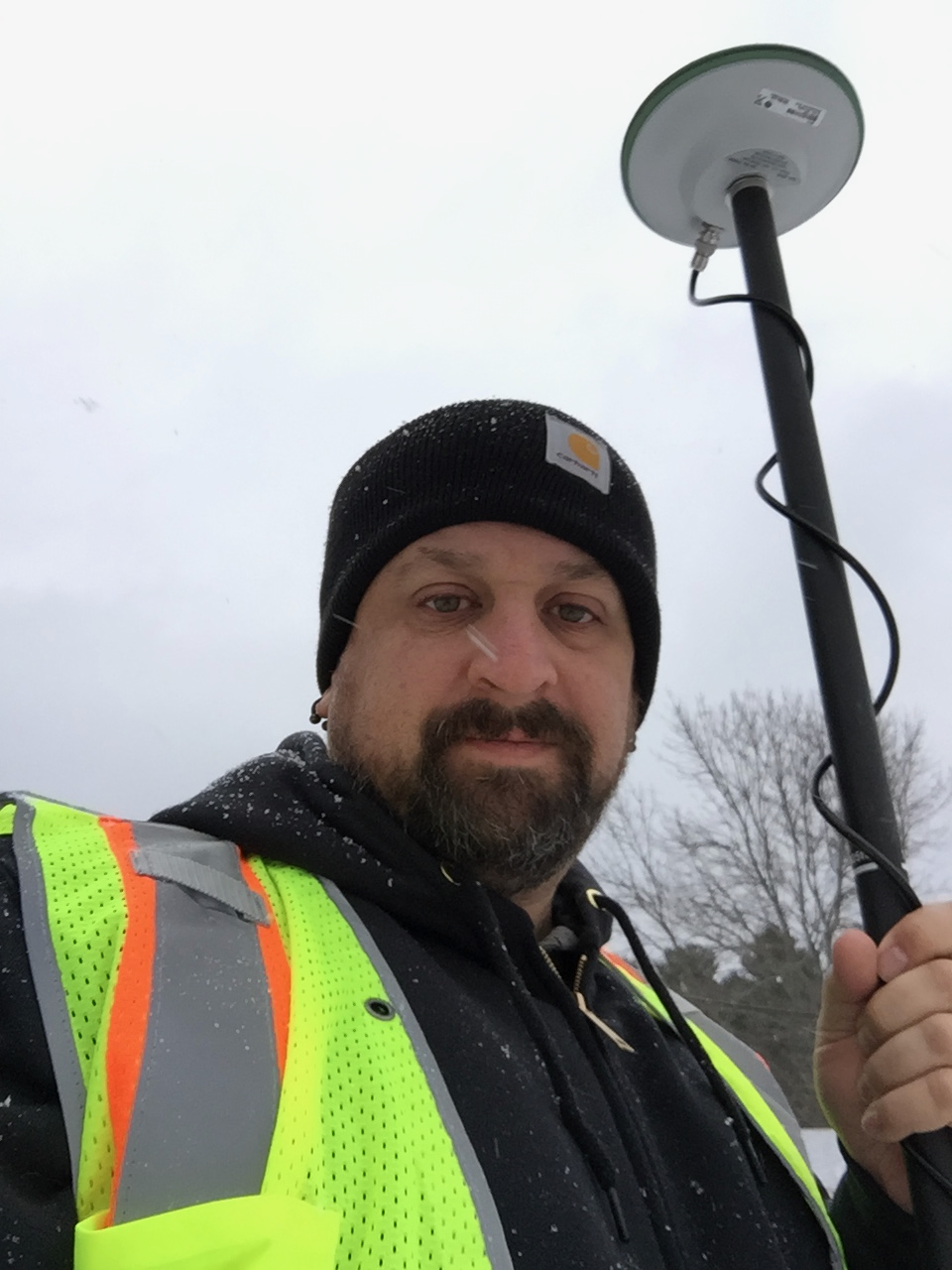 Erich Rainville in high-visibility gear holding a GPS surveying pole during a snowy field visit